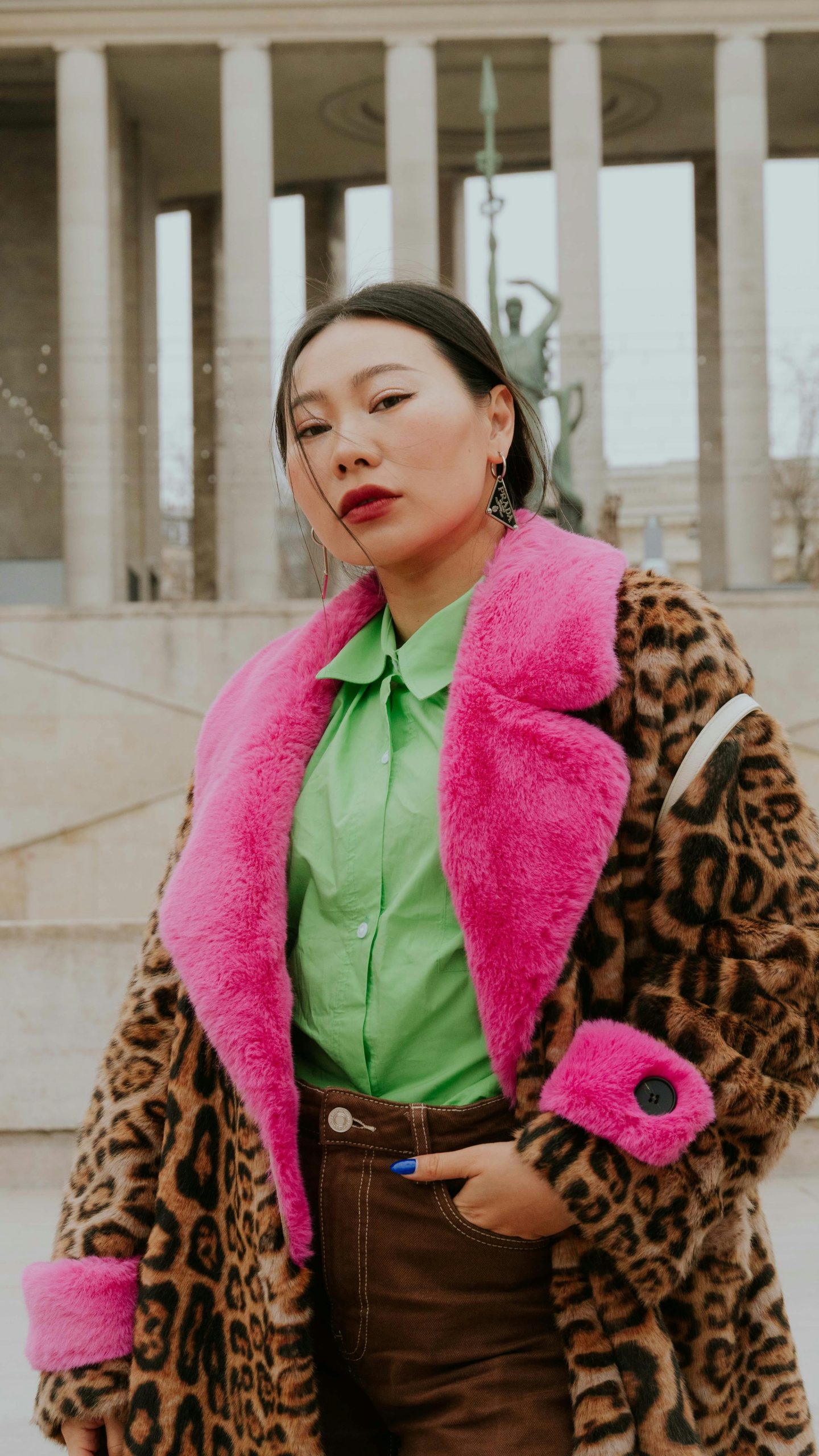 Fashionable woman in leopard print coat with pink fur collar poses confidently outdoors.