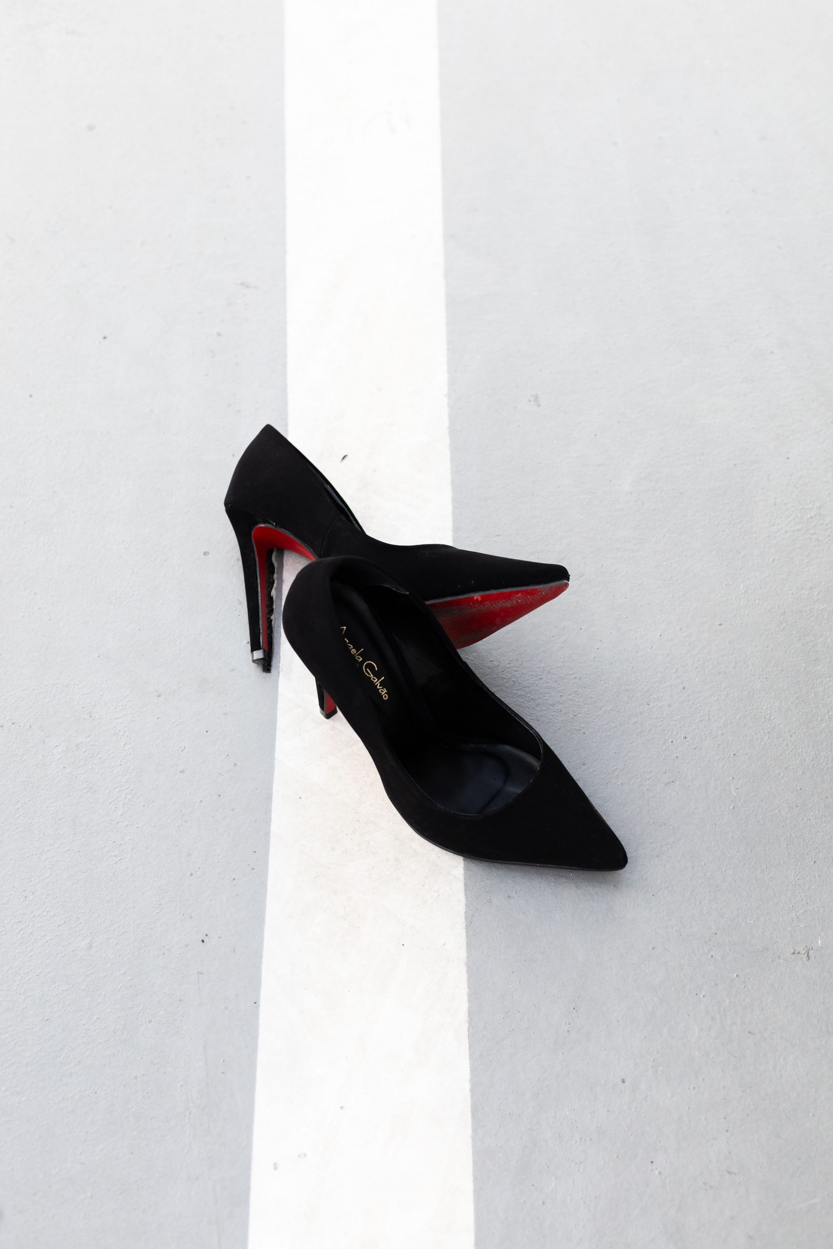 Stylish black high heels with red soles elegantly placed on a gritty urban street line, capturing classic fashion essence.