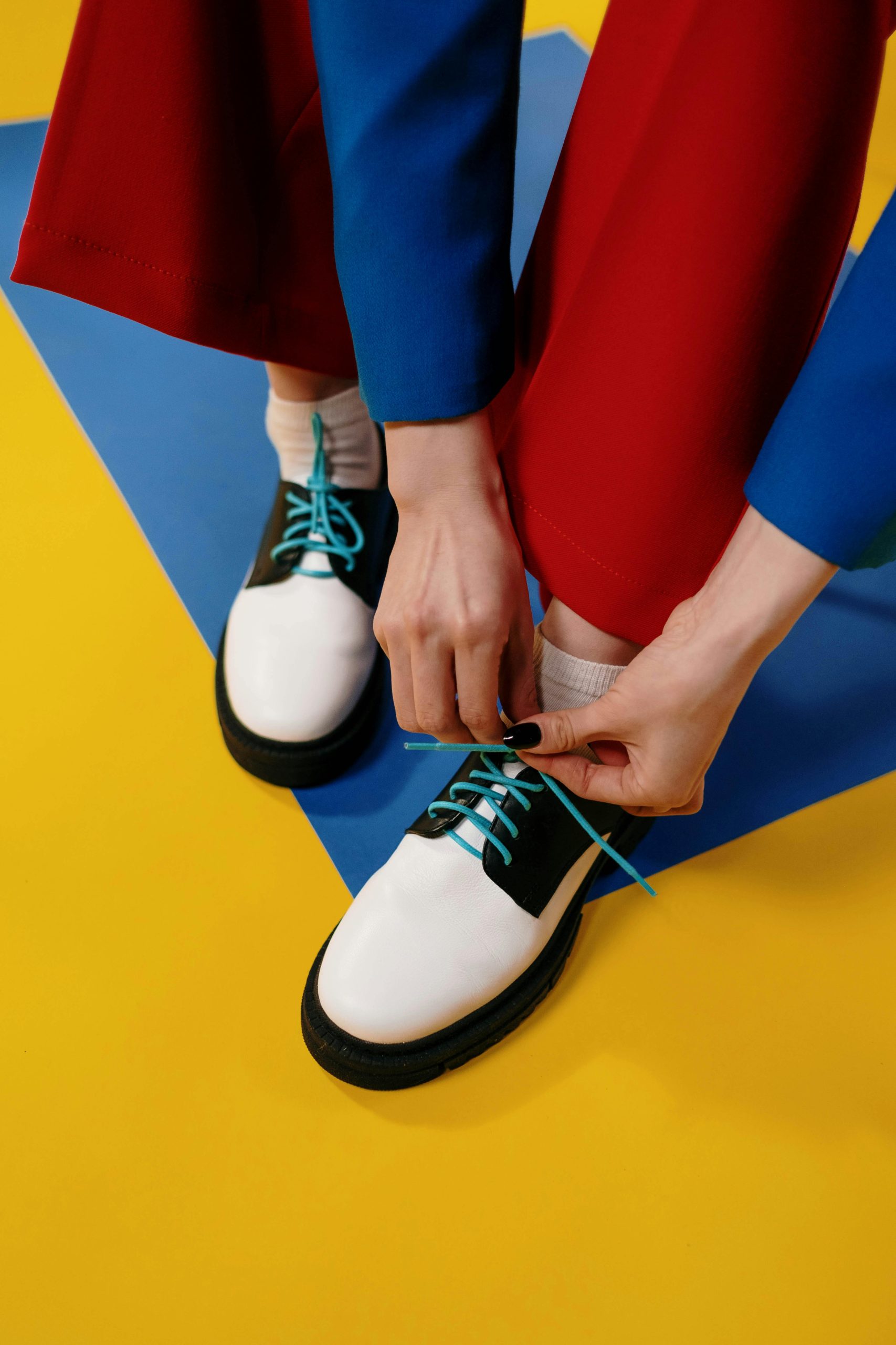 Close-up of hands tying shoelaces on stylish shoes against vibrant background.